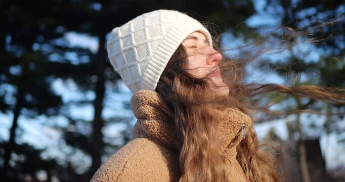 Close-up of a young, attractive woman enjoying the warmth of the winter sun. Wind blows airy hair. Blond female enjoying cold sunny day on nature, outdoor recreation.