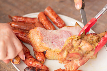 Slicing a cut of meat still raw inside on a plate with sausages. Cutting marinated meat served with browned chorizos.