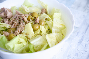 Healthy food. Close up of a bowl of Mediterranean salad made with lettuce, olives, pickled tuna and oregano on a table with a tablecloth