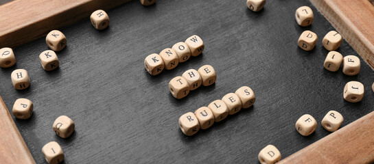 Chalkboard with text KNOW THE RULES and cubes on wooden background