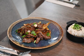 A close-up shot of a traditional Korean dish, Bulgogi, served in a rustic restaurant setting.