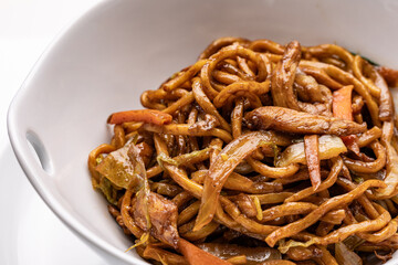A close-up of a white bowl containing Chinese lo mein with chicken and noodles.