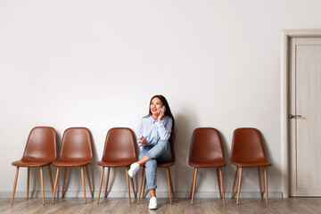 Young Asian woman talking by mobile phone while waiting for her turn in room