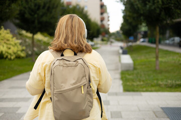 Rear view of young female tourist backpacker with headphones walking on the street. Closeup of...