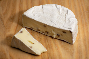 Wheel of creamy camembert cheese topped with nuts, resting on a rustic wooden surface. The rich textures and contrast create an elegant culinary composition