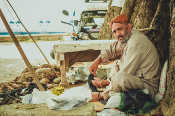 A poor old shoe man cobbler sitting under a tree in a local street shop of Pakistan repairing a shoe