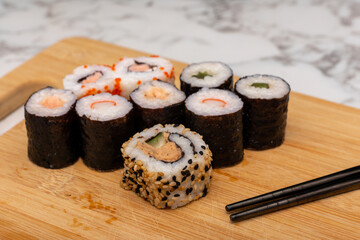 Wooden board with a variety of sushi rolls on it. The sushi rolls are of different colors and sizes, and there are chopsticks next to them. Concept of variety and abundance