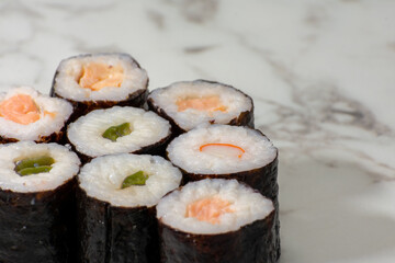 Row of sushi rolls with different fillings, including shrimp, avocado, and cucumber. The rolls are arranged in a neat row on a white countertop