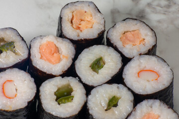 Row of sushi rolls with different fillings, including shrimp, avocado, and cucumber. The rolls are arranged in a neat row on a white countertop