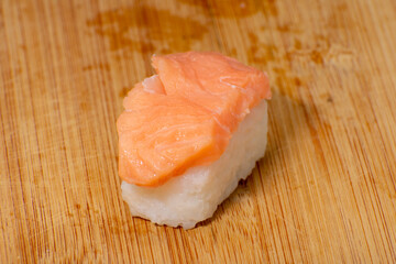 Delicate Nigiri Sake sushi with fresh salmon atop a bed of white rice, presented on a wooden cutting board. A simple yet elegant portrayal of Japanese culinary art with a rustic charm.