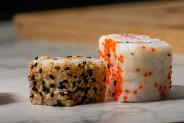 Sushi rolls rest on a white surface, featuring a variety of toppings including salmon, sesame seeds, and vibrant orange fish roe, creating a colorful and appetizing display.