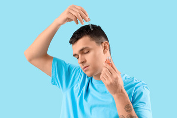 Young man using serum for hair growth on blue background, closeup