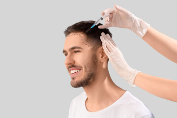 Young man with marked forehead receiving injection for hair growth on light background, closeup