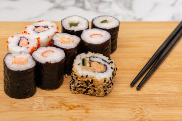 Wooden board with a variety of sushi rolls on it. The sushi rolls are of different colors and sizes, and there are chopsticks next to them. Concept of variety and abundance