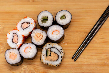 Plate of assorted sushi rolls with chopsticks on the side. The sushi rolls are of different colors and flavors, and the chopsticks are black. Concept of variety and abundance