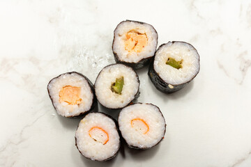 Sushi with a black and white surface. The sushi is arranged in a row and has a variety of colors and textures. Scene is calm and serene, as the sushi is presented in a simple