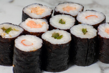 Row of sushi rolls with different fillings, including shrimp, avocado, and cucumber. The rolls are arranged in a neat row on a white countertop