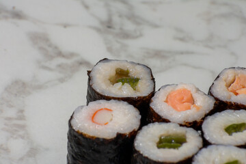 Row of sushi rolls with different fillings, including shrimp, avocado, and cucumber. The rolls are arranged in a neat row on a white countertop