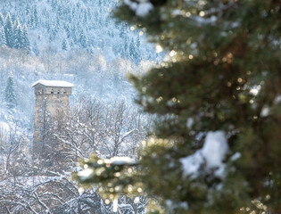 Ancient tower in winter forest with snow-draped trees in Georgia