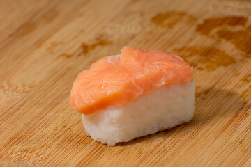 Delicate Nigiri Sake sushi with fresh salmon atop a bed of white rice, presented on a wooden cutting board. A simple yet elegant portrayal of Japanese culinary art with a rustic charm.