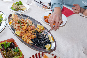 Black risotto and seafood. 
Crop of unrecognizable man serving plate of risotto over dining table with seafood.