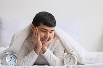 Young man with alarm clocks lying in bedroom, closeup