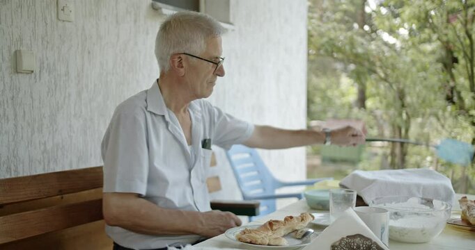 Elderly Man Enjoying a Peaceful Breakfast Outdoors: Savoring Pie and Yogurt on a Sunny Morning