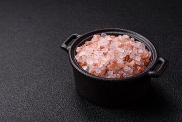 Pink himalayan salt in a black bowl on a dark concrete background