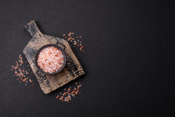 Pink himalayan salt in a black bowl on a dark concrete background