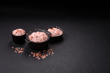 Pink himalayan salt in a black bowl on a dark concrete background