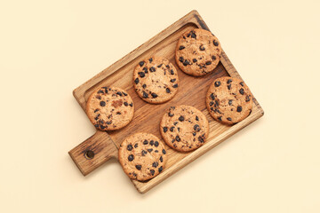 Wooden board of sweet cookies with chocolate chips on yellow background