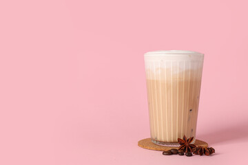 Glass of iced latte with star anise and coffee beans on pink background