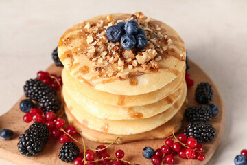 Wooden board of sweet pancakes with different fresh berries and nuts on white background, closeup