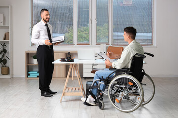 Young lawyer with book and man in wheelchair at office