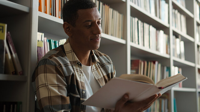 African American man sitting library floor bookcase reading book pleasure hobbies story knowledge learning student turning pages male guy academy study literary university history interesting reader