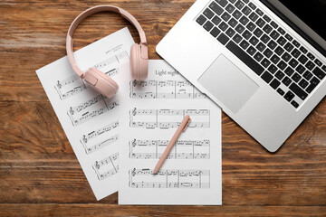 Music sheets with laptop and headphones on wooden background