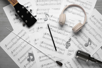 Music sheets with headphones, microphone and guitar on grey wooden background