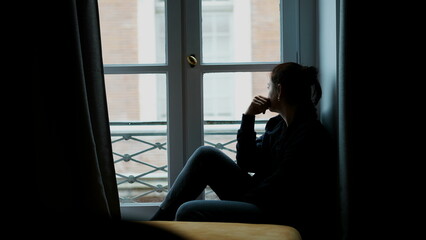 Woman sitting by apartment woman in melancholy. Pensive thoughtful person looking outside