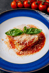Italian lasagna topped with fresh basil and Parmesan on vibrant blue plate, a timeless classic dish