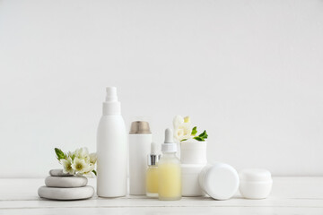 Set of different cosmetic products, spa stones and beautiful flowers on light wooden table