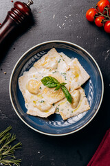 Creamy ravioli garnished with fresh basil leaves served on a blue plate, an Italian culinary delight