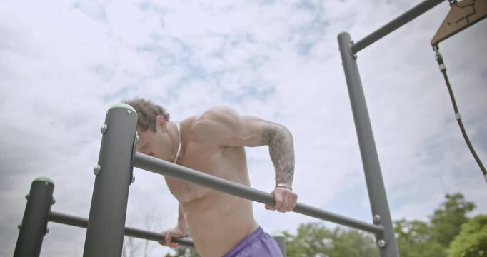 Three athletic people working out on the parallel bars and other outdoor fitness equipment in a park. The video shows fitness, health, and wellness.