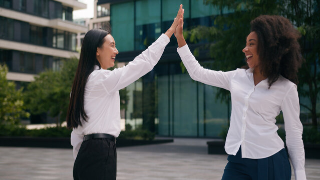 African American Asian Korean women females together happy laughing businesswomen business partners coworkers give high five good teamwork city colleagues smiling talking two people outdoors friends