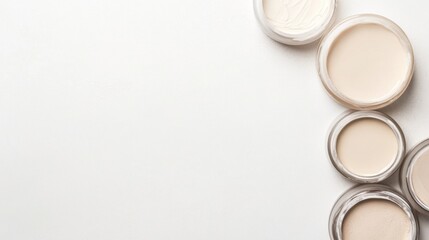 Top view of various skincare creams in small jars on white background.