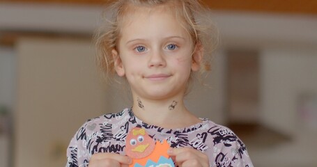 A young child proudly presenting their handmade craft project in a comfortable home environment,...