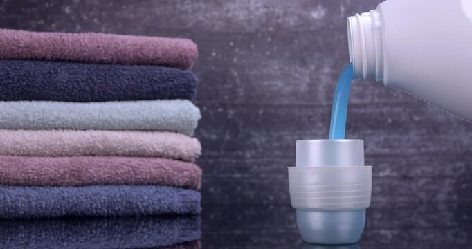 Liquid detergent flowing from the bottle into the container in front of the towels. Laundry and freshness concept. Slow motion 4k