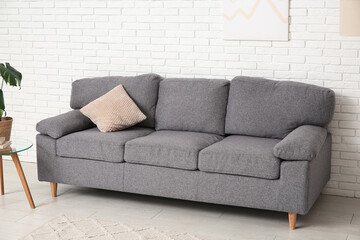 Interior of stylish living room with comfortable sofa, coffee table and houseplant near white brick wall
