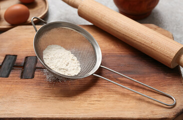 Metal sieve with flour, wooden board and rolling pin on grunge table, closeup