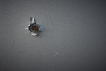 Damage from a small hole in a gray wall revealing a wooden surface beneath