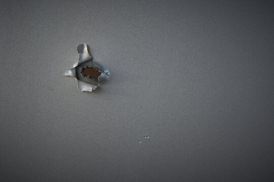 Damage from a small hole in a gray wall revealing a wooden surface beneath